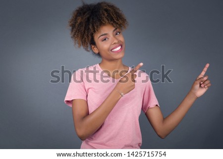 Pretty young African woman with positive expression, dressed casually, indicates with fore finger at blank copy space for your promotional text or advertisement. Adorable woman poses indoor alone