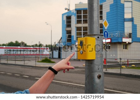 The hand of the girl presses the button of the pedestrian crossing. Yellow button electronic crosswalk. A hand sign indicates a button.                              