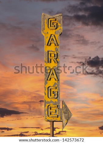 Vintage neon garage arrow sign with sunset sky.