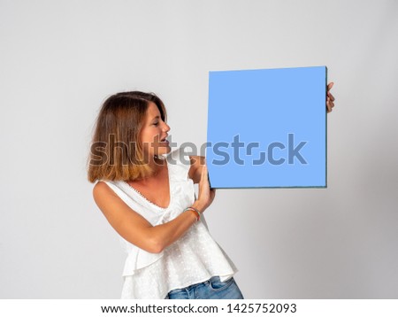 Blonde girl sitting on the floor with white background holding blue pictures to put your text
