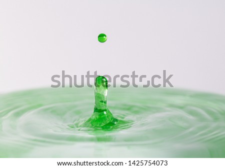 Close up macro photography of a green water drop splashing into water with a light colored white gray background