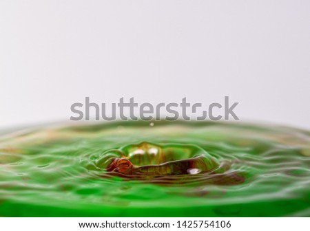 Close up macro photography of a red and green water drop splashing into water with a light colored white gray background