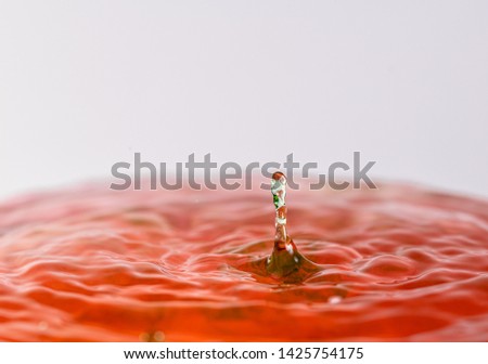 Close up macro photography of a red and green water drop splashing into water with a light colored white gray background
