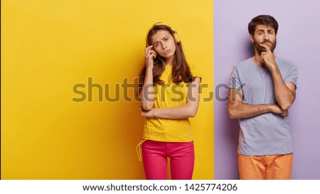 European couple dont speak to each other after quarrel, woman ignores husband listening music in headphones, pensive serious guy holds chin, contemplates about something. Two colored background