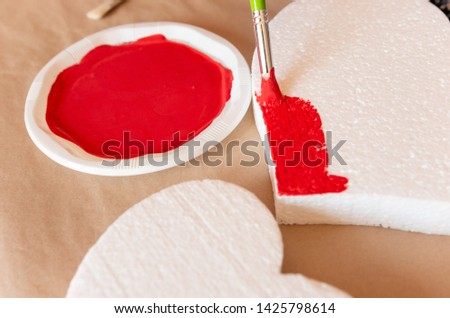 
woman's hand with green brush painting hearts of red
