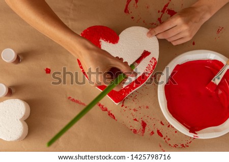 
woman's hand with green brush painting hearts of red