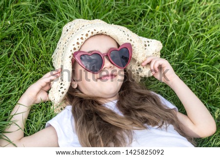 little girl laying in the grass with sunglasses and summer hat. summer time and sunny day