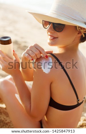 Woman Applying Sun Cream Creme on Tanned  Shoulder. Sun Protection.Sun Cream. Skin and Body Care. Girl Using Sunscreen to Her Skin. Portrait Of Female Holding Suntan Lotion 