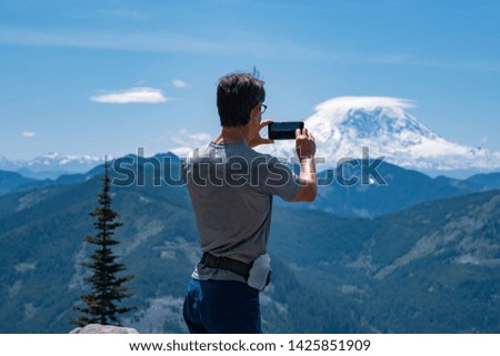 Rear view of man taking photo of a mountain in nature.