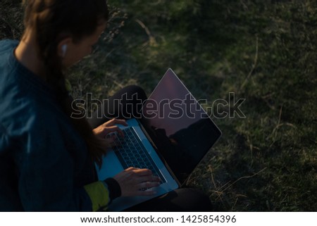 Close view of young woman working on laptop with earphones in the fields 
