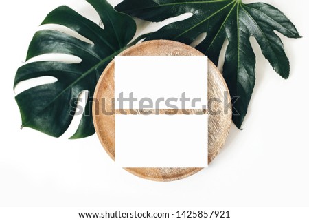 Blank white business cards mockups, wooden plate, aralia and monstera leaf isolated on white table backgound. Modern template for branding identity. Tropical design. Wedding stationery. Flat lay, top 