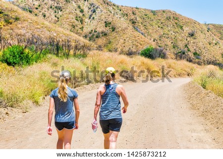 Mother and teenage daughter hike together in Southern California mountain forest on hot summer day on dirt fire road
