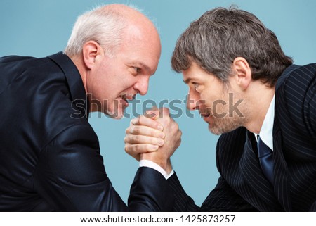 Two determined businessmen going head to head in a challenge for supremacy staring into each others eyes and arm wrestling