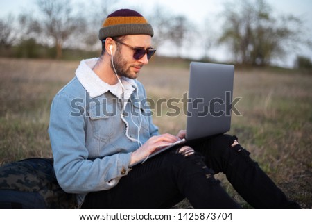 young guy joyfully working on laptop in the green fields