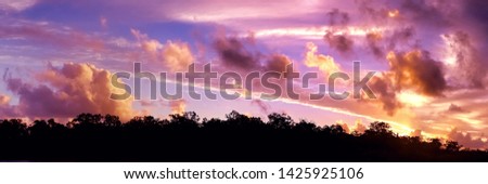 A striking brightly coloured orange cumulonimbus cloudy tropical panoramic sunset cloudscape featuring horizon in silhouette. Queensland, Australia.