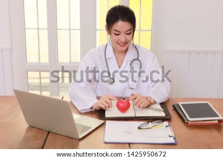  Young woman doctor holding a red heart, in office.
