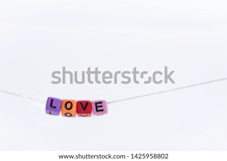 Colorful english alphabet cube with word LOVE hanging on on a string with white paper background.