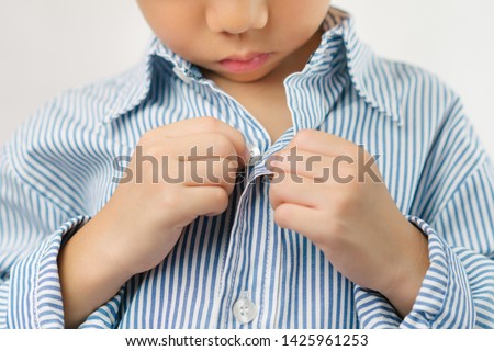 Child Development concept: Close up of a little kindergarten boy's hands learning to get dressed, buttoning his striped blue shirt. Montessori practical life skills - Care of self, Early Education. Royalty-Free Stock Photo #1425961253