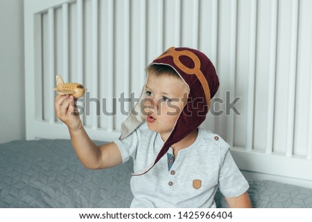 Cute smiling little boy in the cap of the pilot plays on the bed with a small wooden plane. Aviation day.