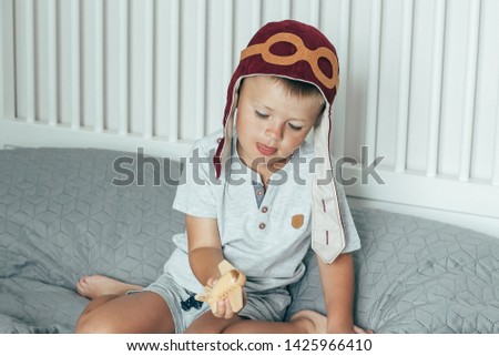 Cute smiling little boy in the cap of the pilot plays on the bed with a small wooden plane. Aviation day.
