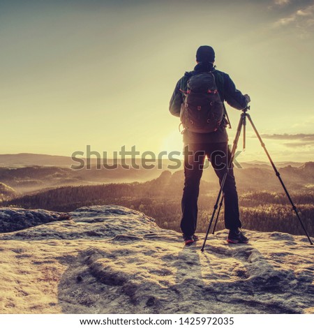 Professional photographer prepares a camera and a tripod before shooting of nature picture on the mountain summit.