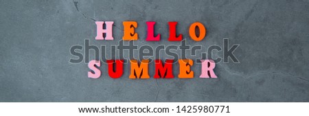 The multicolored hello summer word is made of wooden letters on a grey plastered wall background.