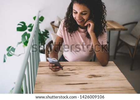 Good looking African American female student dressed casually holding mobile phone and typing messages, positive woman communicating with friends via social networks using high-Internet connection
