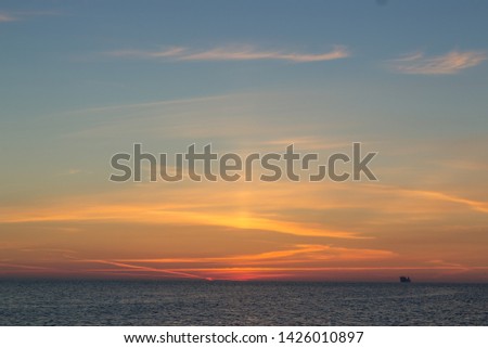 Seascape photos of a morning, golden sunrise at the sea and ocean. Small, little clouds and orange sunlight with dark water.