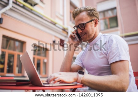 Positive Caucasian man in classic eyewear calling to customer service for consultancy about media application for editing pictures using international roaming for phoning via mobile application