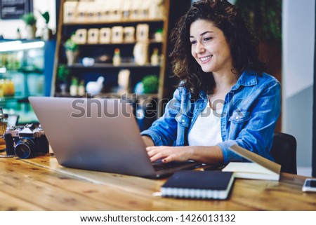 Happy female photographer editing photo from vintage camera on desktop via application on laptop computer, positive smiling hipster girl feeling good during working process on modern netbook