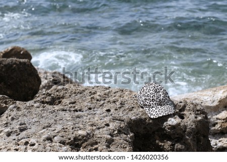 Cap on the beach. Cap left on the rocky shore near the sea. Tropical vacation and relax travel concept. Leopard print cap. Mediterranean sea, Turkey. Forgotten thing.   