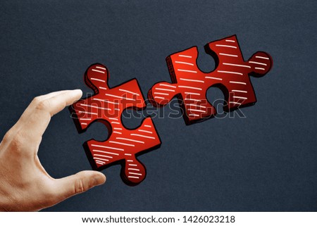 Hands holding drawn red puzzle pieces on subtle paper background. Teamwork and success concept