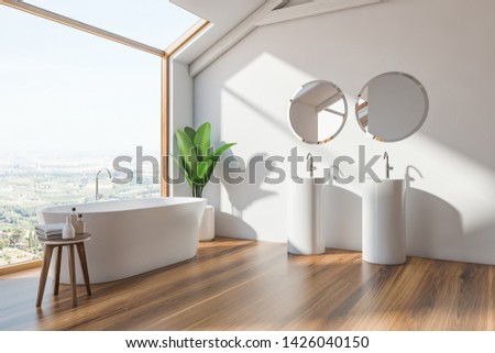 Corner of loft Scandinavian style bathroom with white walls, wooden floor, white bathtub standing near window and double sink with round mirrors. 3d rendering