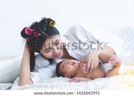 Young Asian mother with her 2 month old baby on the bed, child is crying