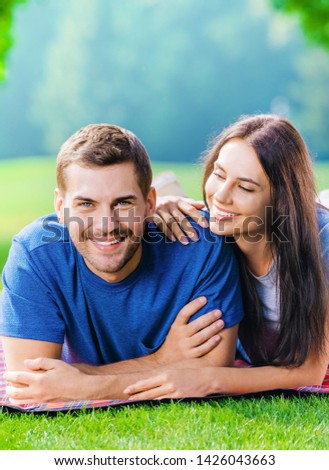 Picture of young happy smiling couple in love, lying together on a picnic blanket, outdoors at summer time.