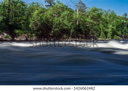 Touristic Landscape Scene of Burleigh Falls in Selwyn Ontario Canada featuring silky,soft and smooth high level water rapids, exotic pink limestones , blue sky background with fresh green leaves fores