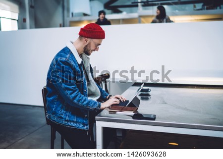 Side view of positive male blogger writing publication review for sharing sitting at modern coworking space with high speed internet connection, concept of freelance people and networking