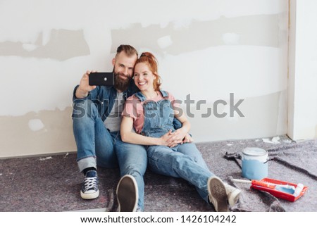 Smiling loving young couple posing for a selfie on the floor of their unfinished living room during DIY renovations