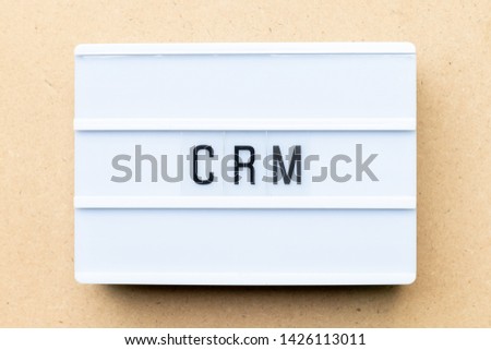 White lightbox with word CRM (Abbreviation of Customer Relationship Management) on wood background