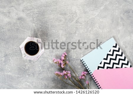 Flat lay composition with coffee cup, pink flowers, paper notebook on concrete surface. Top view female home office desk. Cozy morning breakfast concept.  
