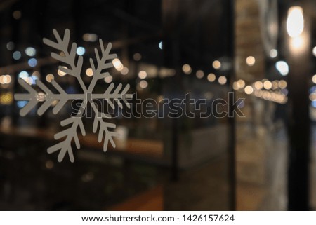 White sticker of snow flake on the glass wall with the reflection of bokeh light. As the exterior decoration of Christmas event. Selective focus.