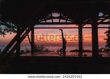 Man practising a headstand with sunset background. Yoga retreat with bamboo hut and red, orange sky. Handstand balance. Shot in Montanita beach, Ecuador.