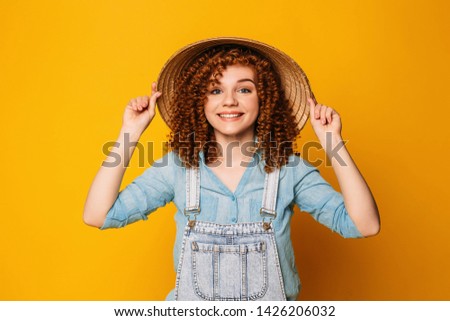 Red-haired curly woman in a straw hat is laughing, on a yellow background. funny travel, summer trip