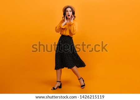Amazed young woman posing in straw hat. Studio shot of shocked girl dancing on yellow background.