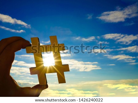 closeup of the hands of a young caucasian man  holding a wooden sign in the shape of a hash tag symbol against the sky, with some blank space. hashtag