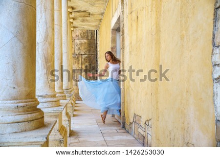 Girl running away in dance looking back, wearing in blue airy skirt in ancient ruins walls and columns in Macao