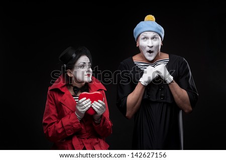 two funny mimes holding red heart isolated on black background