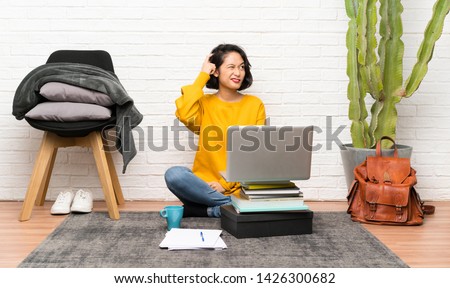 Asian young woman sitting on the floor having doubts and with confuse face expression Royalty-Free Stock Photo #1426300682