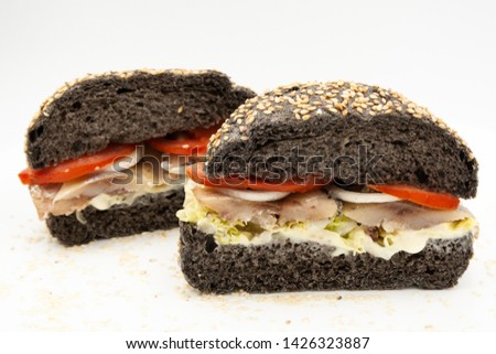 black hamburger with herring and fresh tomato and fresh salad, sandwich, close up