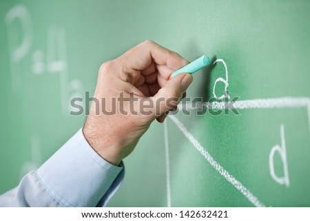 Closeup of mature teacher's hand writing alphabet on greenboard in classroom